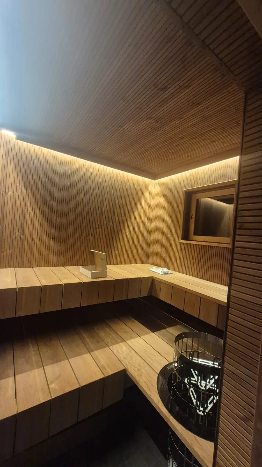 Puinen sauna, jossa on penkit, kiuas ja epäsuora valaistus.