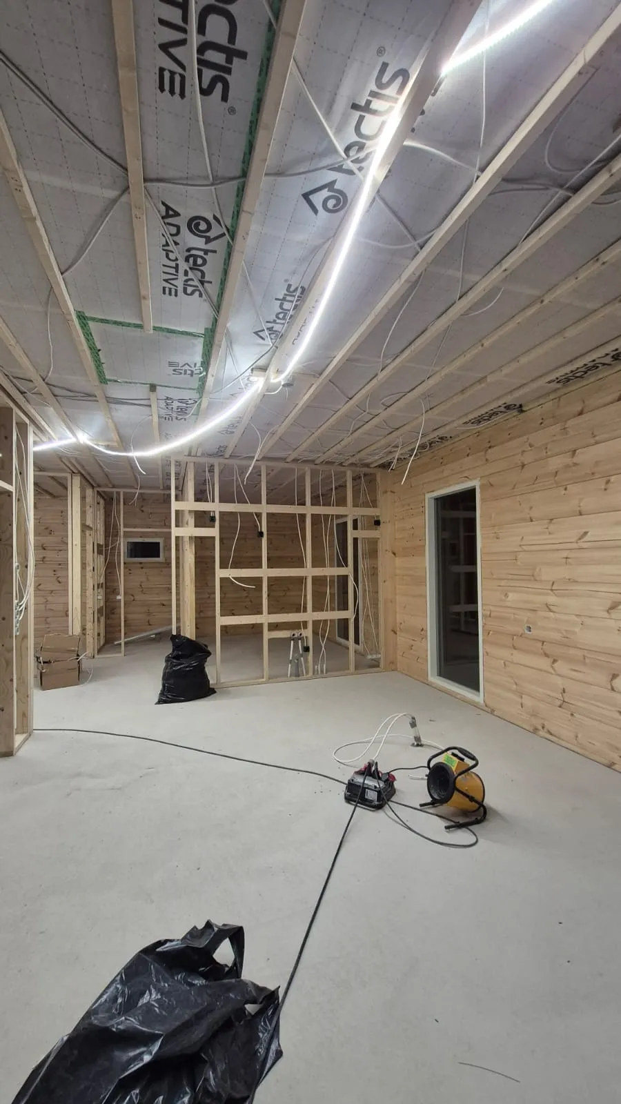 Rakenteilla oleva huone, jossa on puupanelointi, valaistus ja työkaluja lattialla.