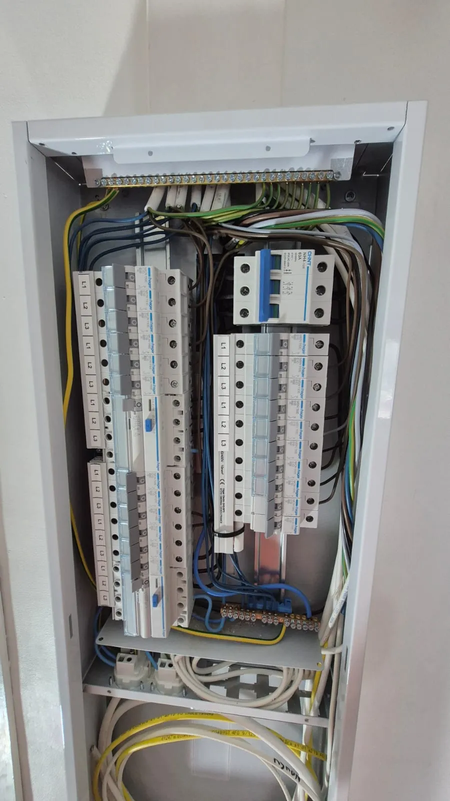 Kuva sähkökeskuksesta, jossa näkyy johdotuksia, sulakkeita ja liittimiä valkoisessa metallikotelossa. Valoisa ja tekninen.